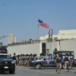 Personel keamanan berjaga di luar konsulat AS di Karachi pada 1 Maret 2026 selama bentrokan dengan Muslim Syiah saat mereka mencoba menyerbu gedung tersebut setelah kematian pemimpin tertinggi Iran Ayatollah Ali Khamenei di tengah serangan AS-Israel. Asif Hassan/AFP via Getty Images